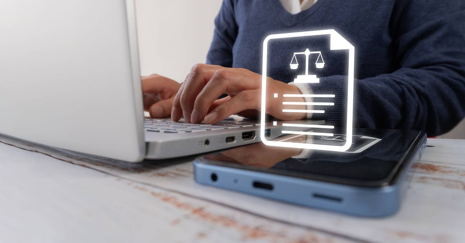 Enterprise-vs.-Small-Business-Licensing-Management-Software Person typing on a laptop with a glowing digital document and scales icon representing the comparison of licensing contract management software.